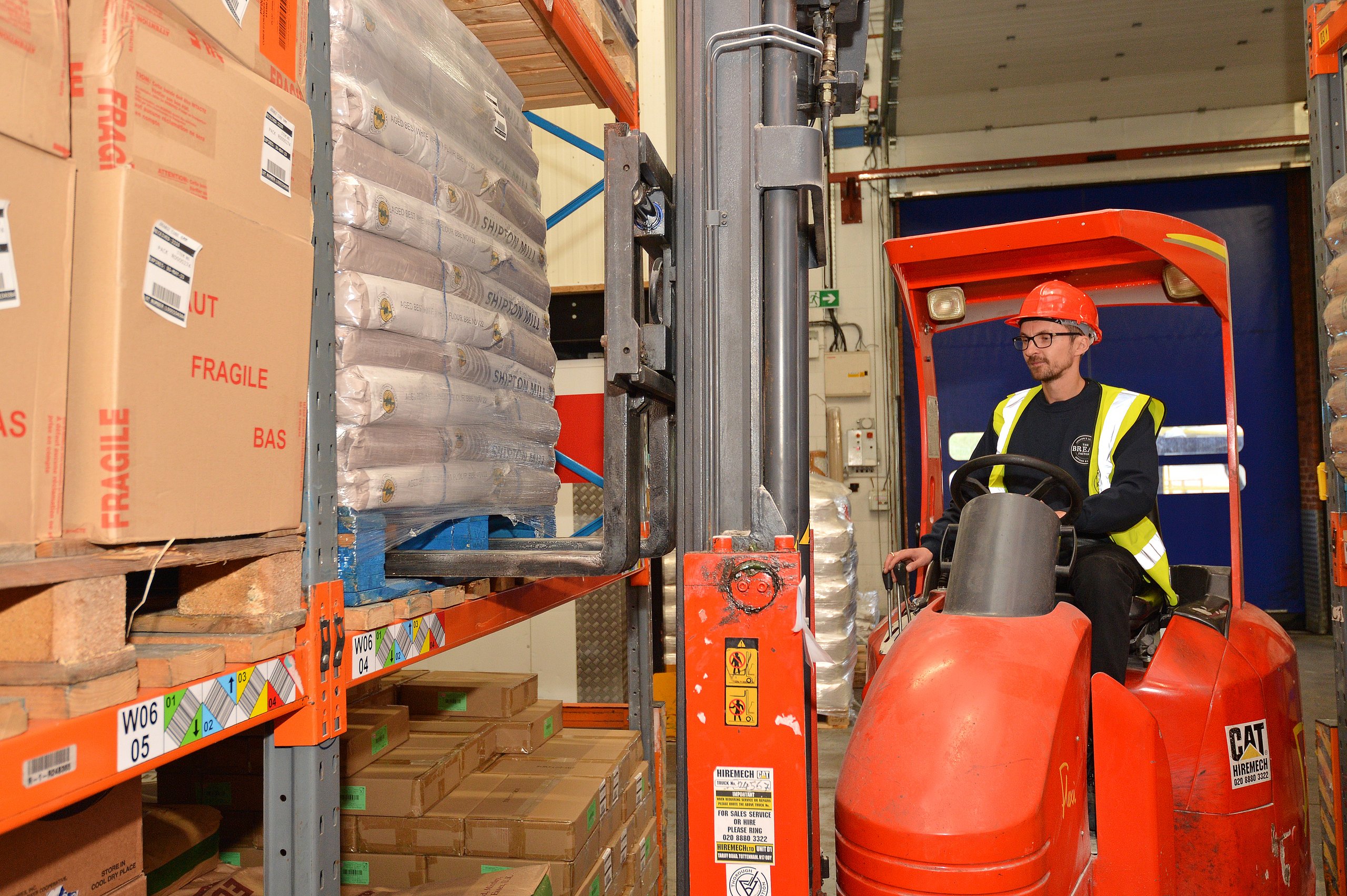 Forklift operator in a warehouse, moving pallets of flour and boxes.
