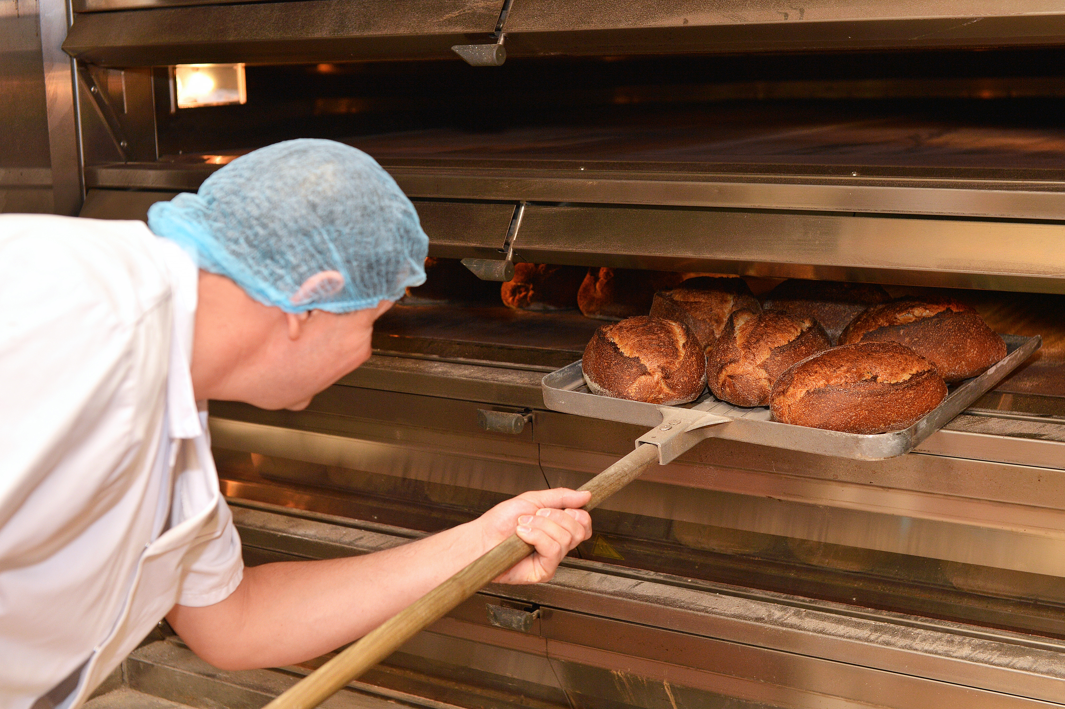 Baker removing bread from oven.