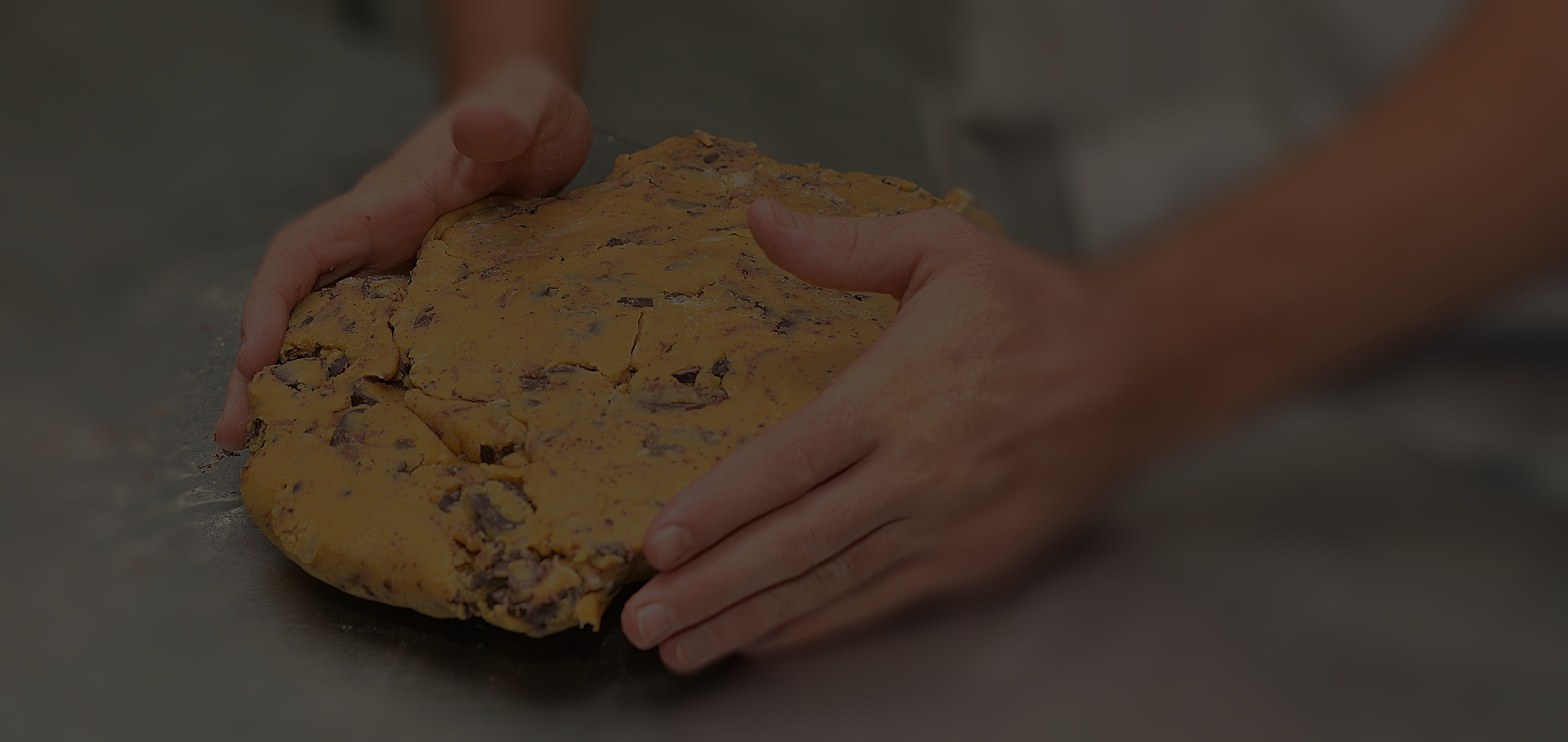 Hands holding a ball of cookie dough with chocolate chips.