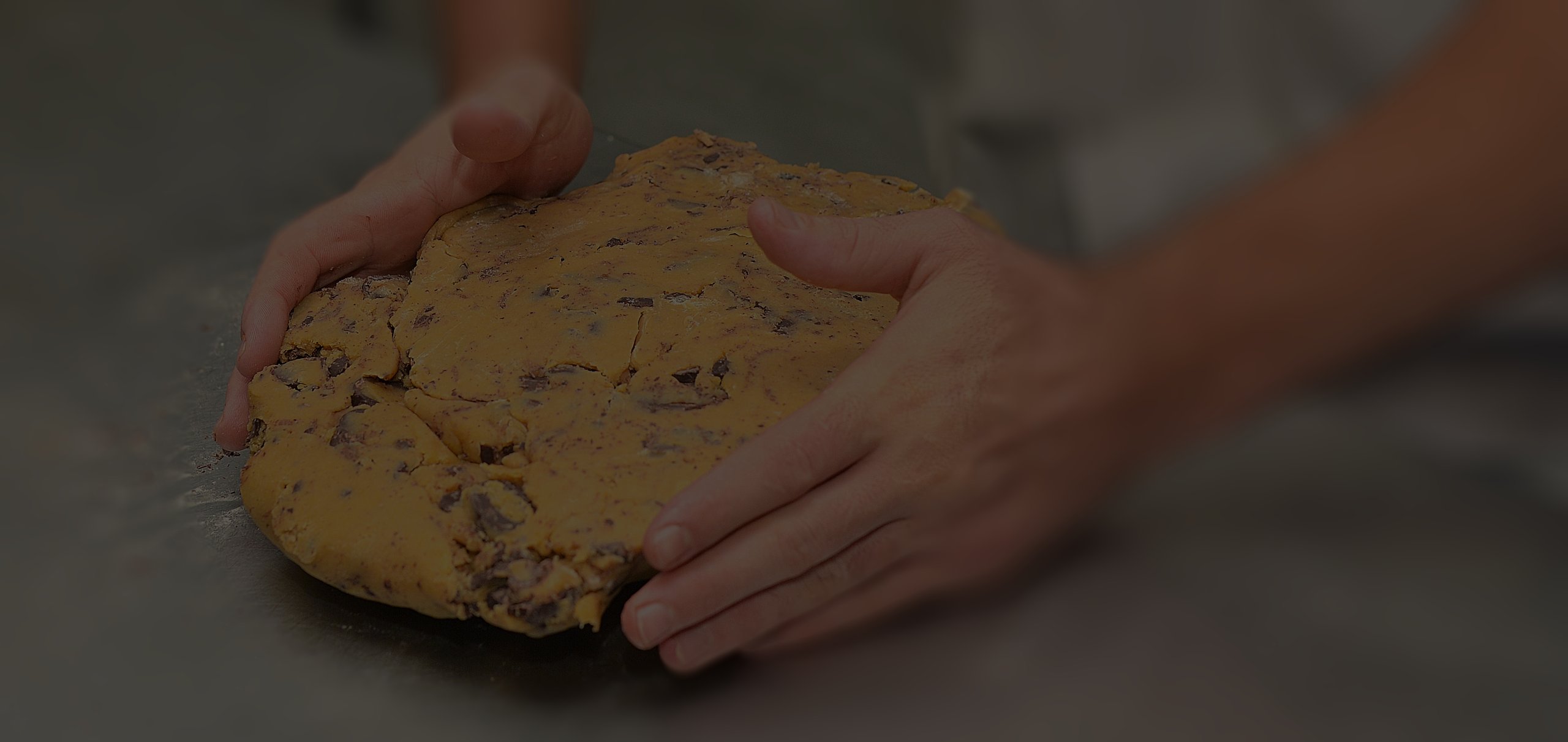 Hands holding a ball of cookie dough with chocolate chips.