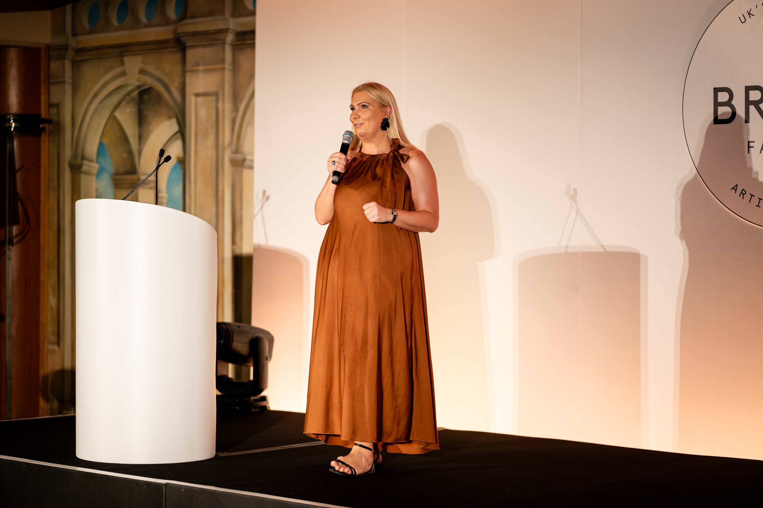 Woman speaking at a podium, holding a microphone.