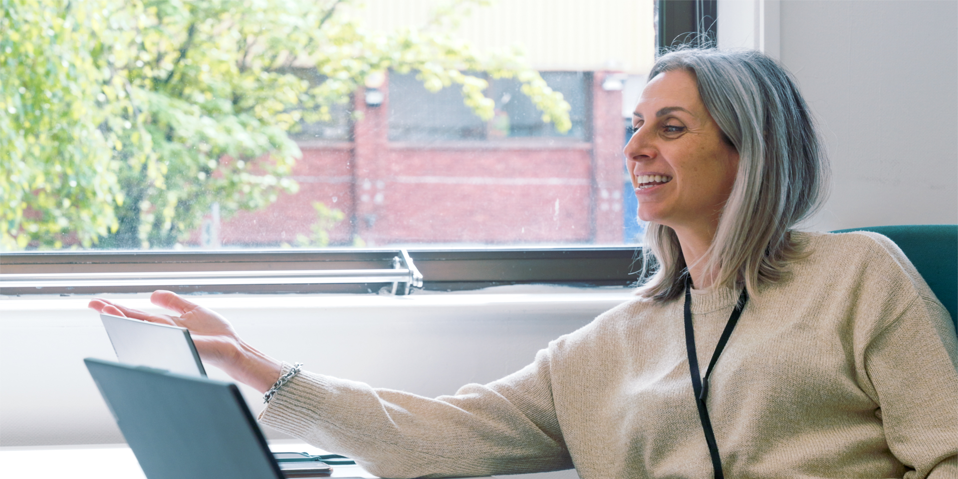 Woman with gray hair smiling, gesturing near laptops.
