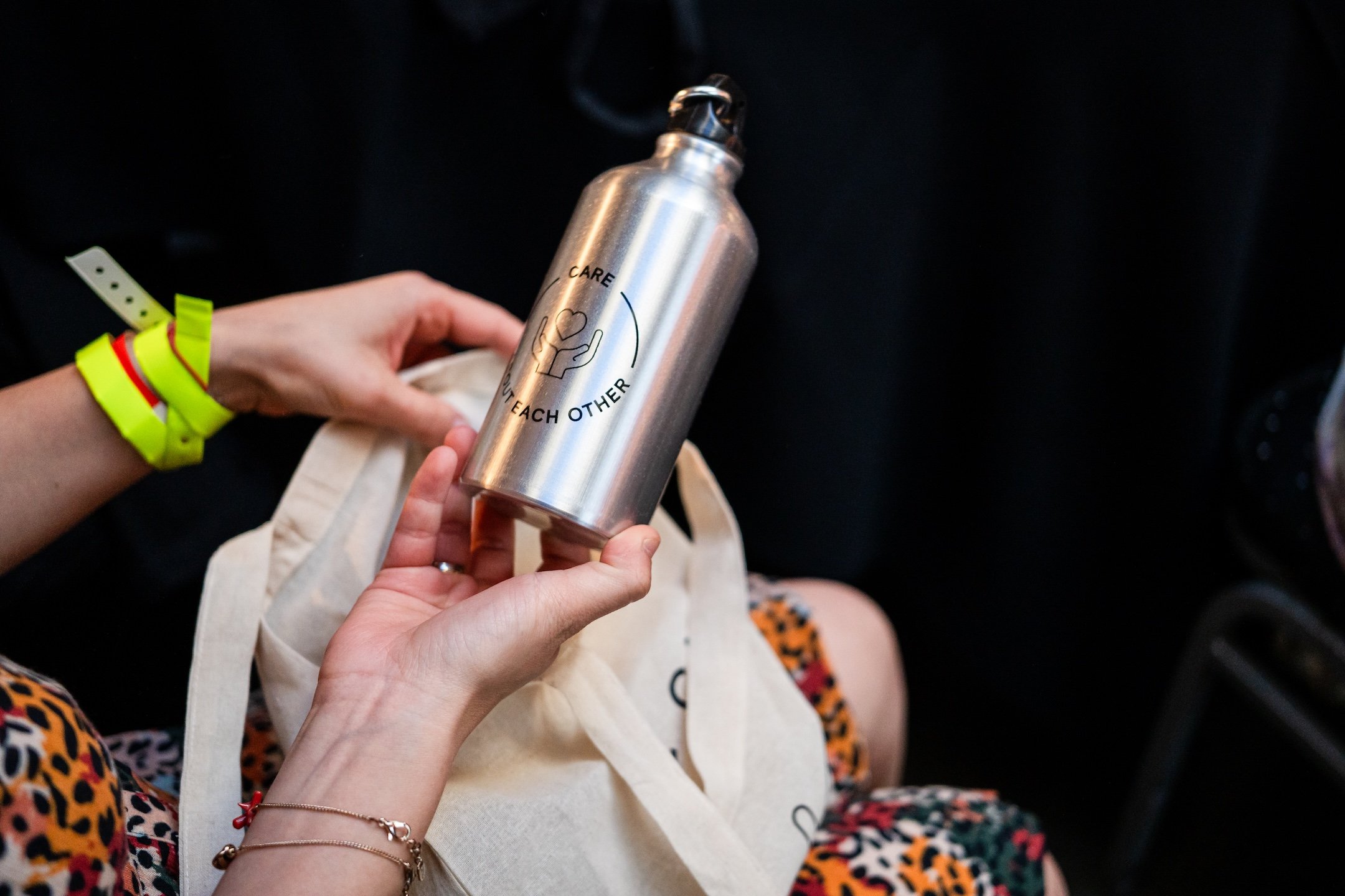Person holding a water bottle with "Care Each Other" text.
