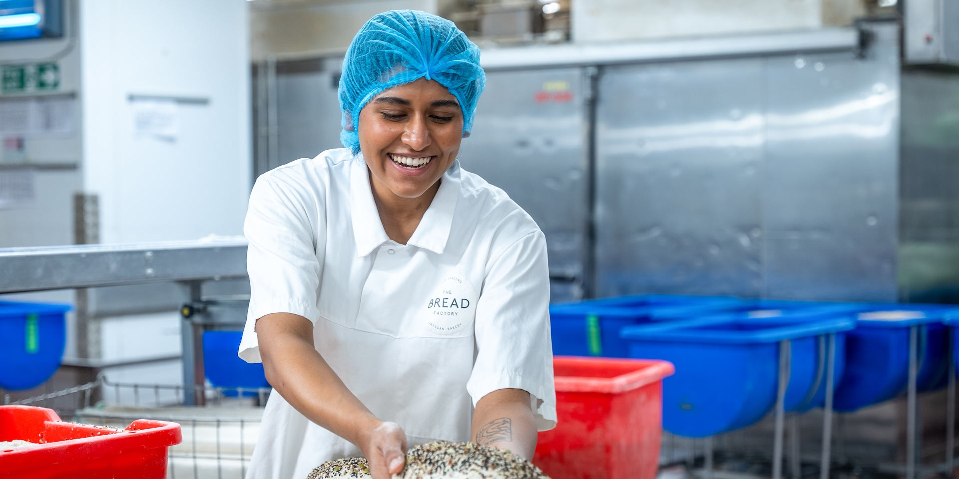 Baker smiling, holding bread, wearing hairnet and uniform.