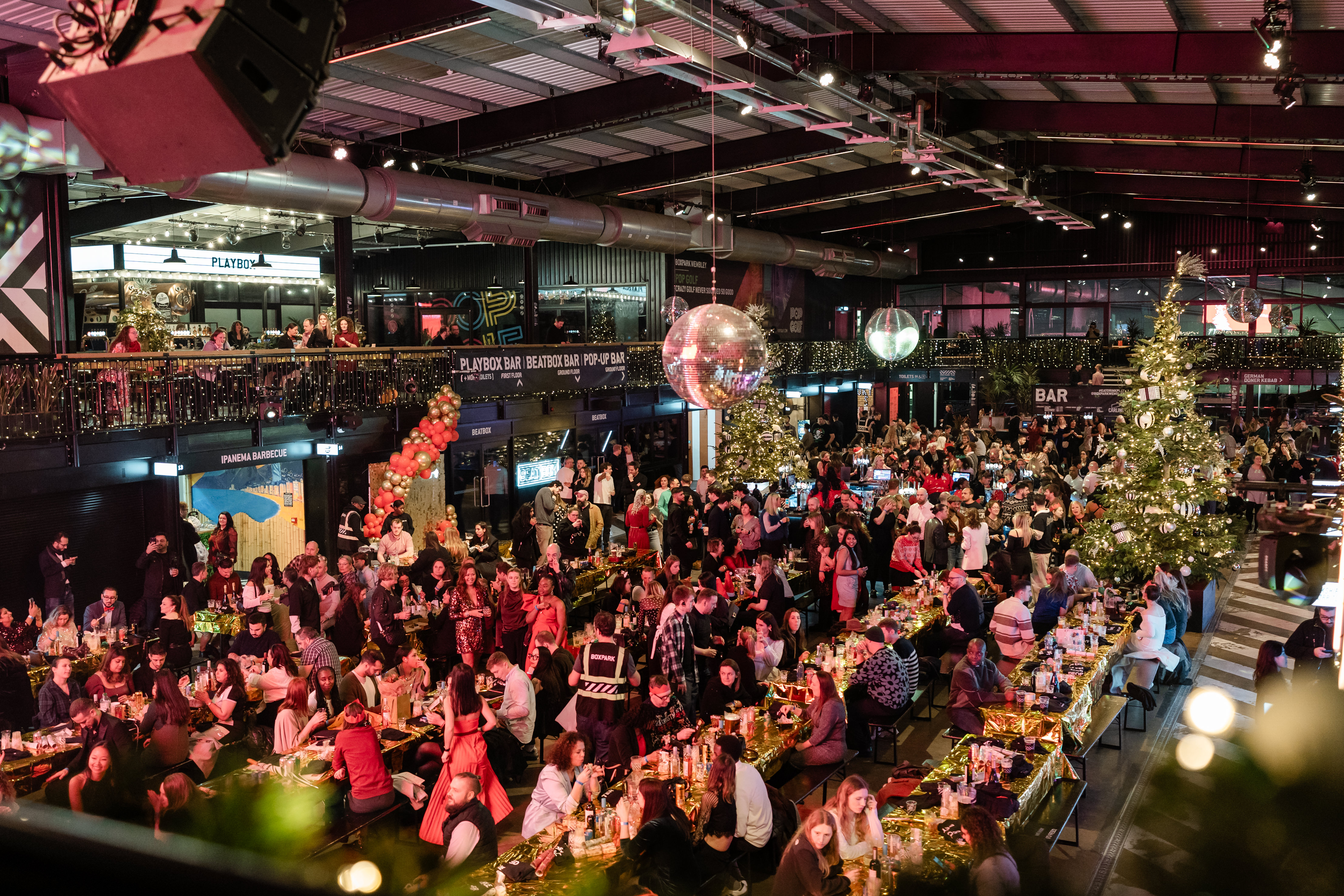 A crowded indoor venue with a Christmas tree, disco balls, and people dining at tables, likely a holiday party.
